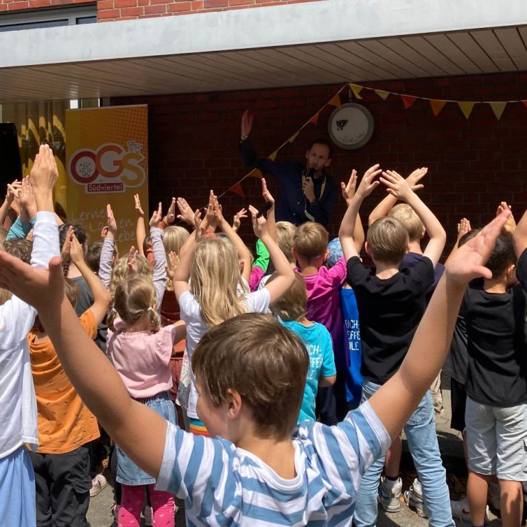 Kinder feiern begeistert vor einer Bühne und bunten Dekorationen.